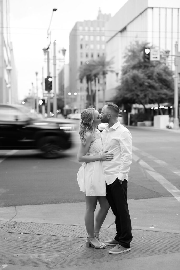 Couple embracing and kissing in Downtown Phoenix while car rushes behind them