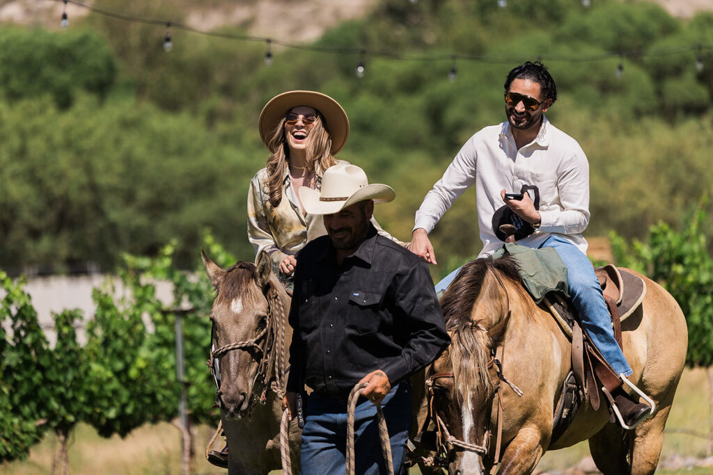 couple laughing while riding horses at vineyard