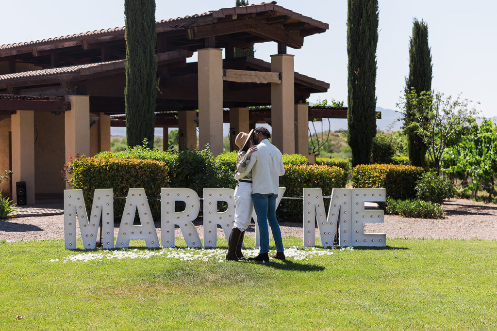 couple kissing in front of marry me sign at vineyard