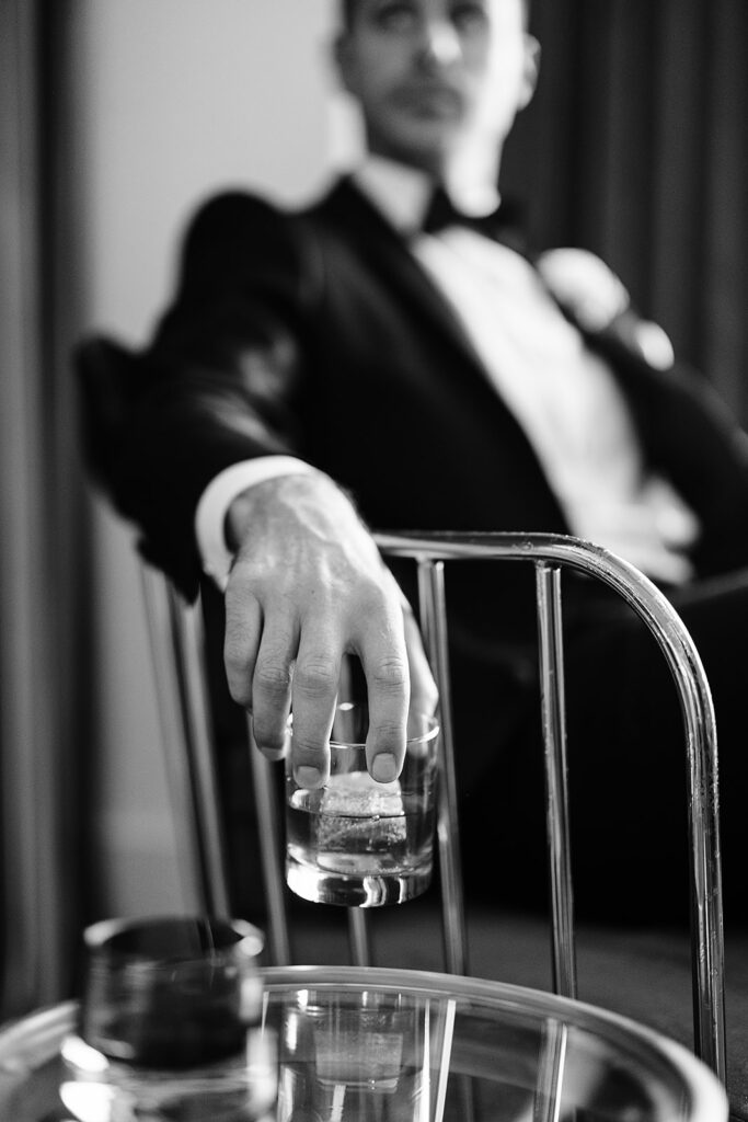 black and white image of groom holding glass of whiskey in suit