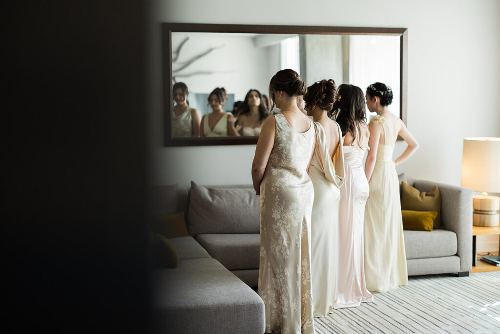 bridal party poses with back to bride in hotel room for first look of bride