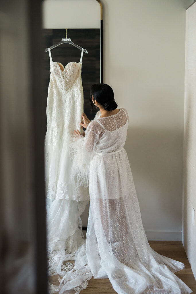 bride looks at wedding dress in hotel room in bridal robe