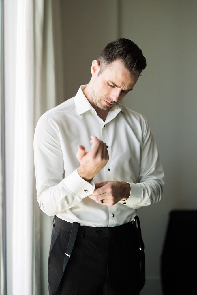 Groom finishes putting on cufflinks on wedding day in hotel room